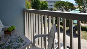 Een balkon met een tafel, stoelen en een schaal fruit. Achtergrond met gebouwen en bomen.