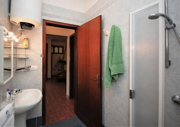 Un baño con lavabo, espejo, toallero, ducha y una puerta que da a otra habitación.