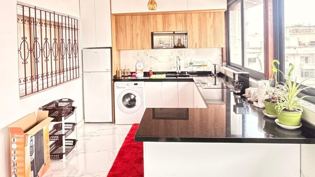 A modern kitchen with a central island, wooden ceiling beams, and a large window providing a view of the city. - Large and beautiful app, large stad ibnoubatouta 15mm Tangier Airport (Tanger)