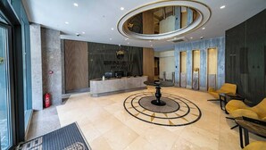 Un hall d’entrée moderne avec un comptoir d’accueil, un espace salon circulaire et un grand miroir au plafond.