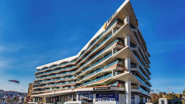 Un hôtel moderne doté de nombreux balcons, d’une enseigne bien visible indiquant le « Benesta Centre », et surplombant un ciel d’un bleu éclatant.