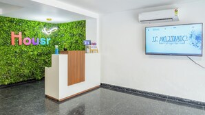 A reception area with a green wall, a wooden reception desk, and a television displaying 'Housr' and 'IC. MALLITANIC!'. - Housr 46 M2K Corp Near Park Hospital (Gurugram)