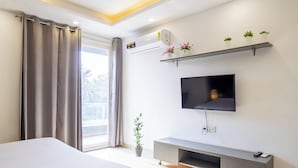 A modern hotel room with a bed, a TV mounted on the wall, a grey console table, and a potted plant. - Housr 46 M2K Corp Near Park Hospital (Gurugram)
