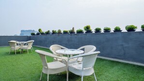 A rooftop terrace with a round table and wicker chairs, surrounded by potted plants and a view of the city skyline. - Housr 46 M2K Corp Near Park Hospital (Gurugram)