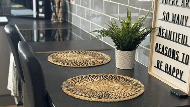 A kitchen counter with two woven placemats, a potted plant, and a motivational sign. - 4 Bed Apartment in Warwick (Warwick)