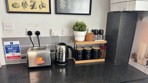 A kitchen counter with a toaster, kettle, and spice jars, along with framed botanical prints on the wall. - 4 Bed Apartment in Warwick (Warwick)