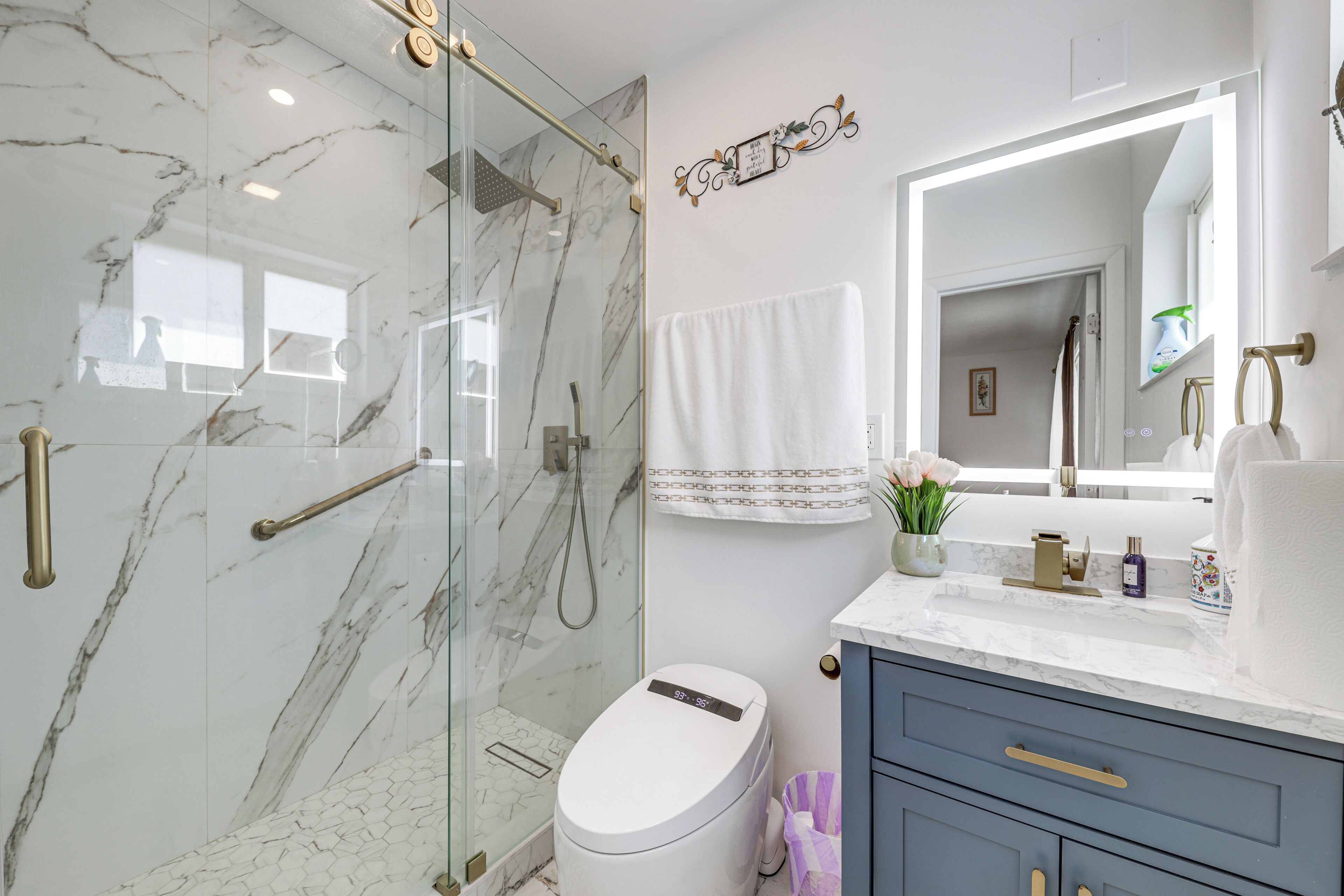 Et moderne badeværelse med en brusekabine i glas, et hvidt toilet og en vask med marmorbordplade.
