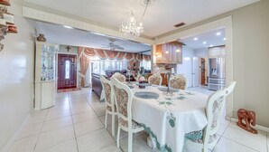 A dining area with a chandelier, white chairs, and a table set for six.