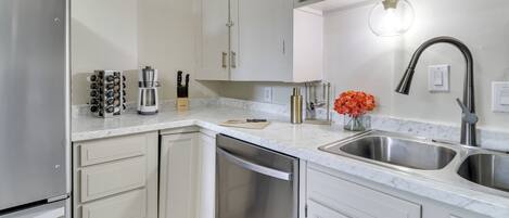 A modern kitchen with white cabinets, stainless steel appliances, and a marble countertop.