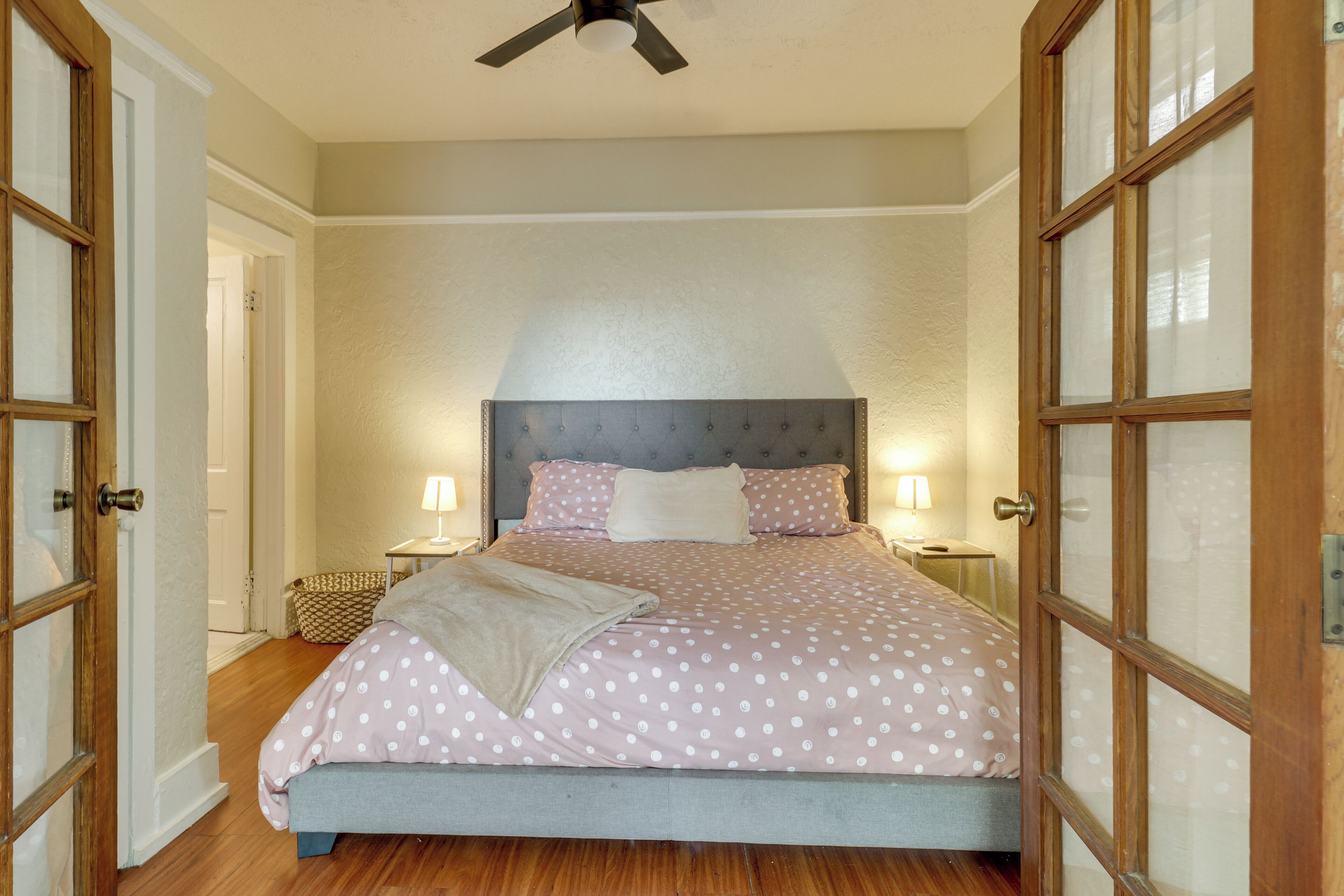 A bedroom with a bed, two bedside tables, a ceiling fan, and a window with wooden frames.