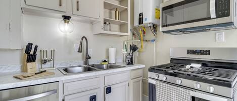 Una cocina moderna con armarios blancos, un lavamanos de acero inoxidable, un microondas integrado y una estufa a gas.
