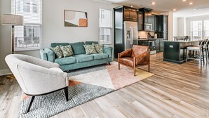 A modern living room with a sofa, a chair, and a kitchen area with a refrigerator and microwave. - 2 Mi to Uptown Charlotte: Townhome w/ Balconies! (Charlotte)