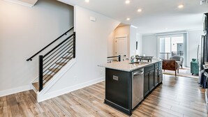 A modern kitchen with a central island, wooden flooring, and a staircase with black railings. - 2 Mi to Uptown Charlotte: Townhome w/ Balconies! (Charlotte)