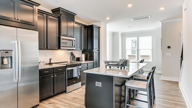 A modern kitchen with dark cabinets, stainless steel appliances, and a central island with bar seating. - 2 Mi to Uptown Charlotte: Townhome w/ Balconies! (Charlotte)