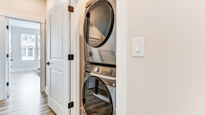 A laundry room with two stacked washers and dryers, a wooden floor, and a white door leading to a hallway. - 2 Mi to Uptown Charlotte: Townhome w/ Balconies! (Charlotte)