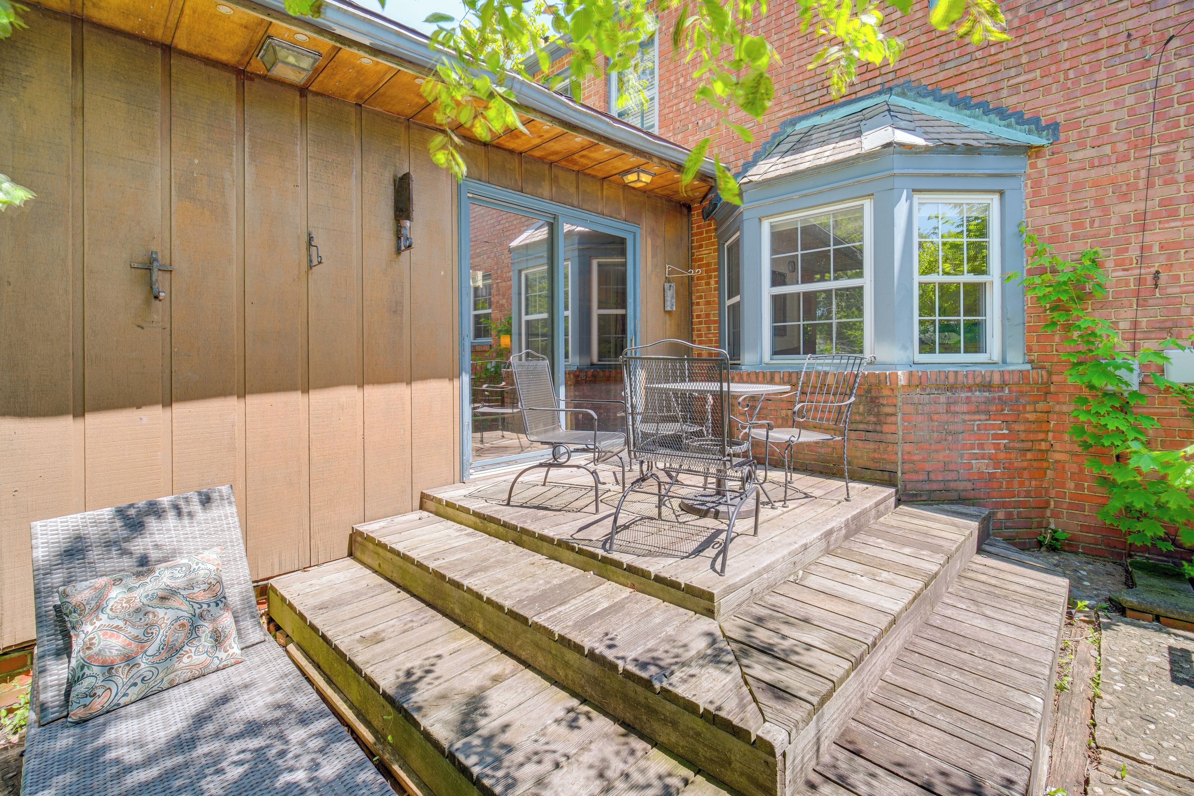 A wooden deck with outdoor furniture, a covered patio area, and a brick building with a blue window.