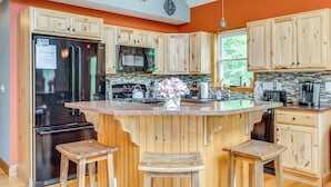 A kitchen with wooden cabinets, a stainless steel refrigerator, a microwave, and a large island with stools. - Ski, Hike & Fish: Chalet w/ Hot Tub in Conway (North Conway)