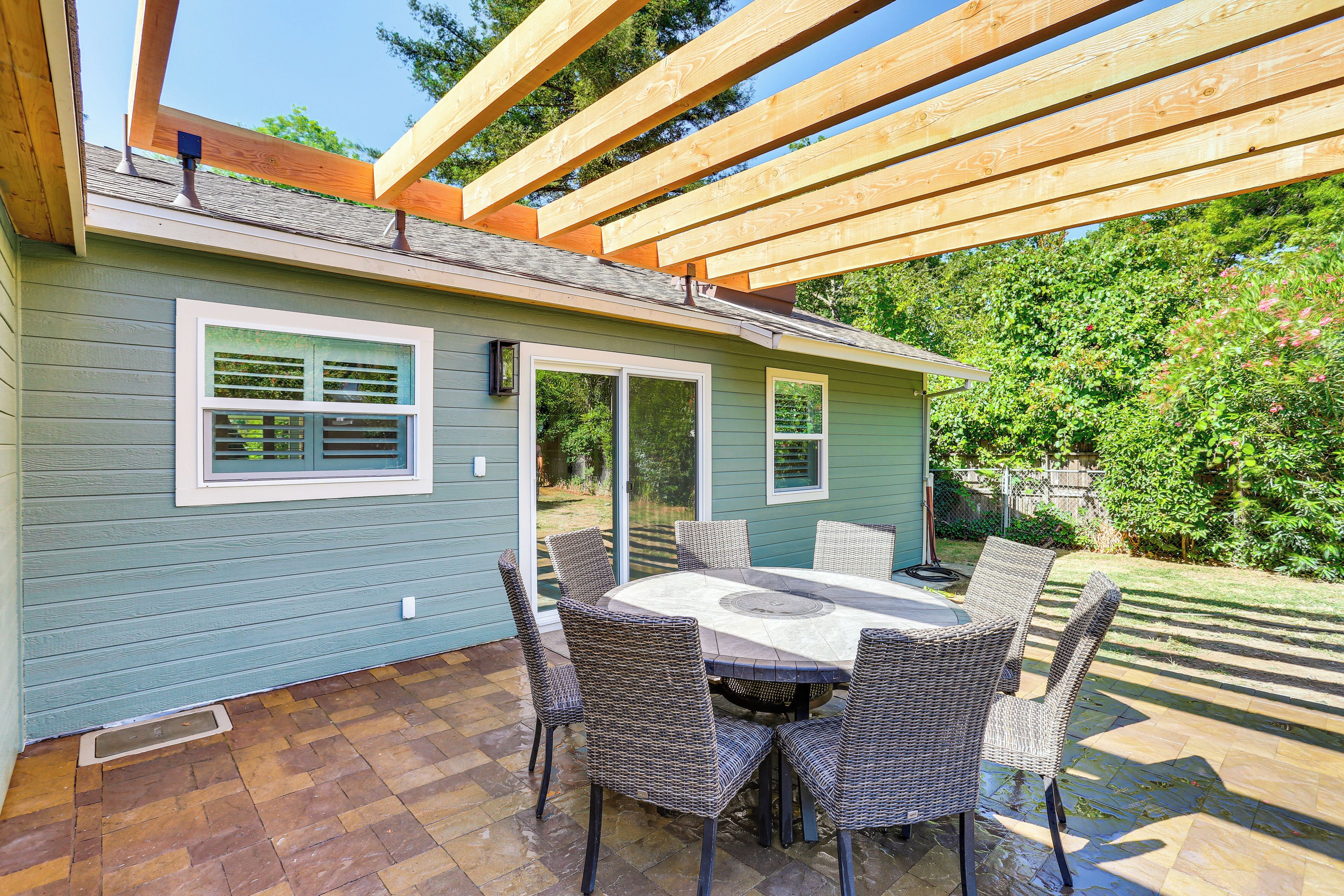 Un patio cubierto con una mesa y sillas, una pérgola de madera y una casa de fachada verde.