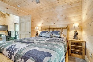 Un dormitorio de cabaña de madera con una cama, dos lámparas de noche, una mesita de noche y un aparador.