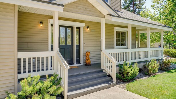 A two-story house with a front porch, a front door, and a small bear statue on the steps.