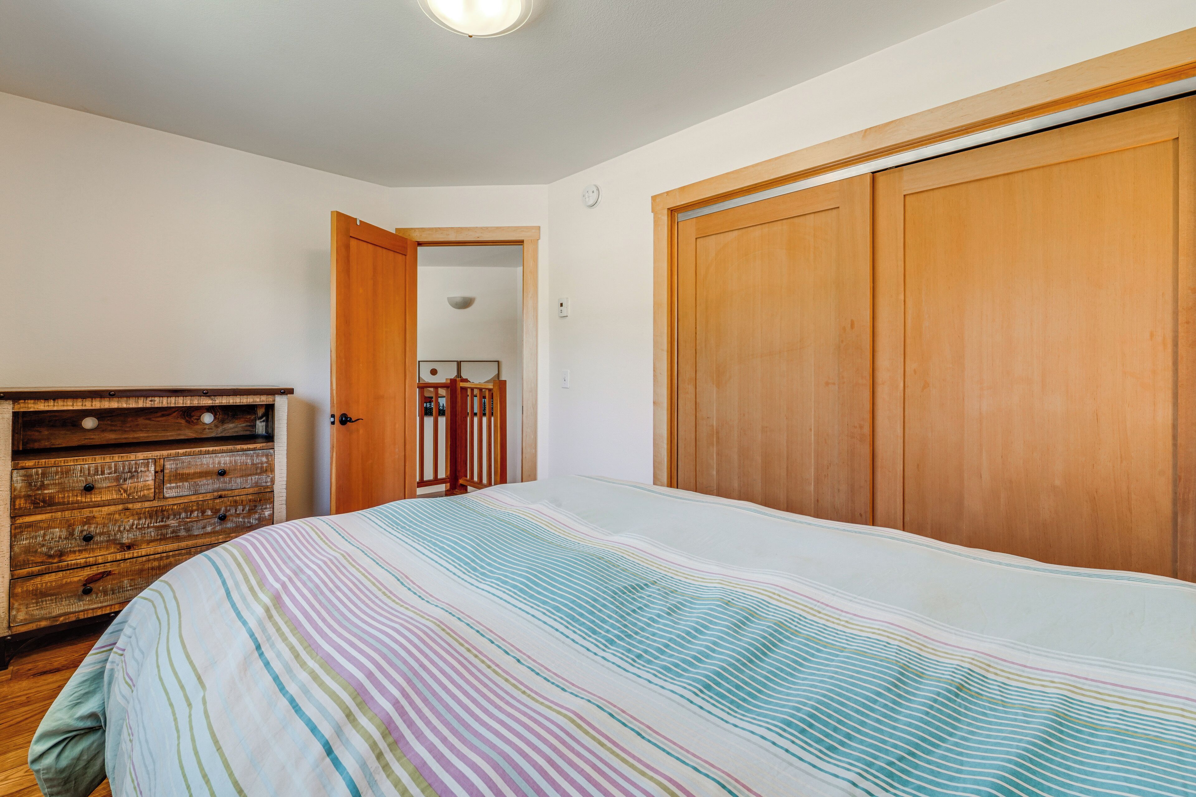 Quarto com cama, guarda-roupa de madeira e cômoda.