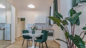 Una cocina moderna con armarios blancos, encimera de mármol y un comedor con mesa blanca y sillas verdes.