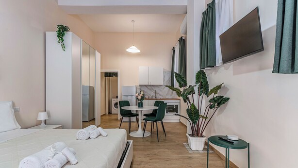 Habitación de hotel con cama, una mesita con sillas, televisor en la pared y una planta en maceta.