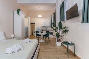 Une chambre d’hôtel avec un lit, une petite table et des chaises, un téléviseur fixé au mur et une plante en pot.