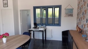 Un comedor con una mesa de madera, sillas azules, una ventana con persianas, un radiador y un papel tapiz estampado.