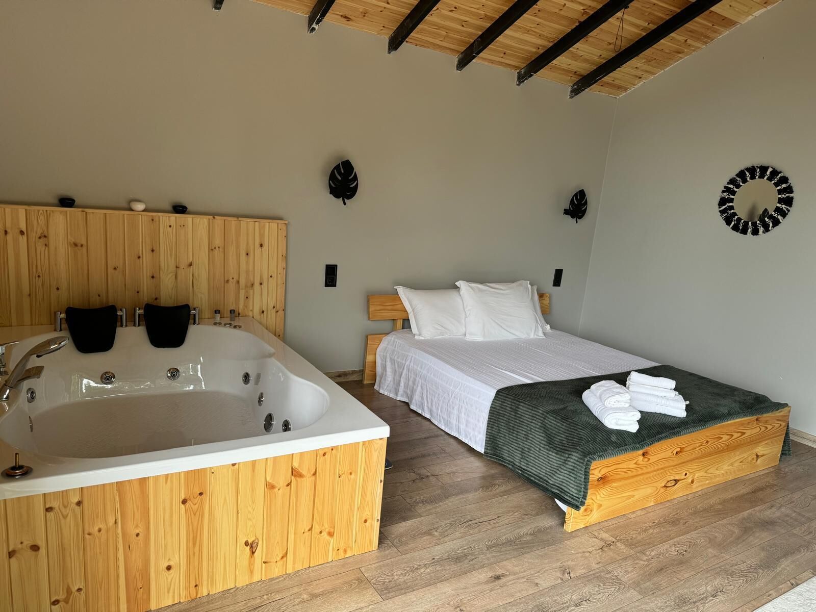 Una habitación con techo de madera, una bañera grande, una cama con ropa de cama blanca y una manta verde.