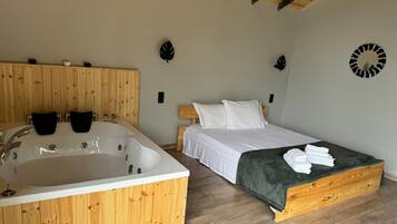 Una habitación con techo de madera, una bañera grande, una cama con ropa de cama blanca y una manta verde.