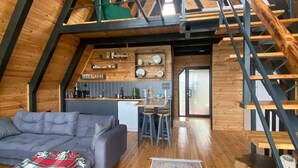 A loft-style room with a wooden floor, a gray sofa, a staircase, and a kitchen area with wooden cabinets and a countertop. - Ordu Bungalov Loın Du Monde (Persembe)
