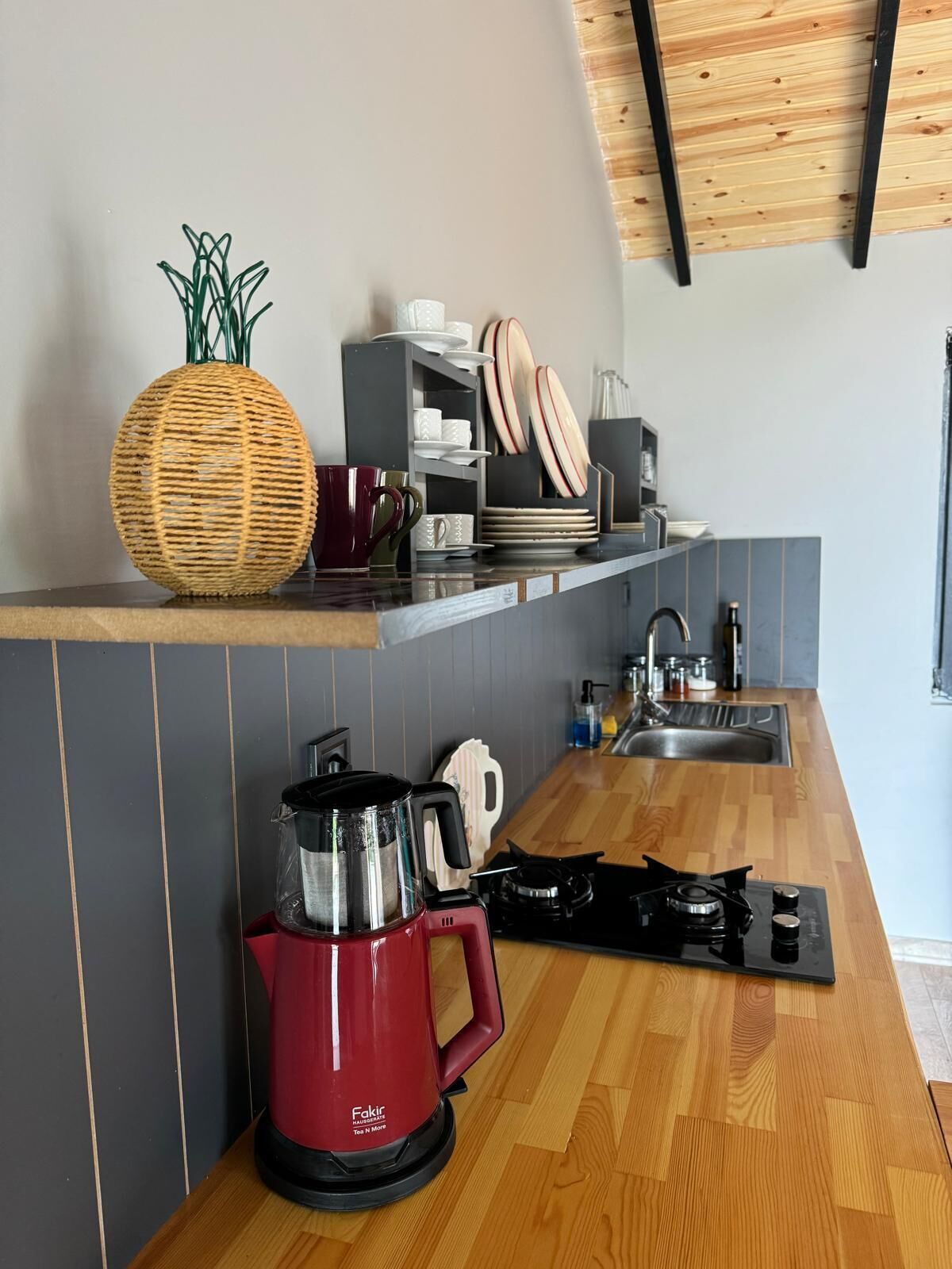 A kitchen with a red coffee maker, a woven basket, and a shelf with plates and cups.