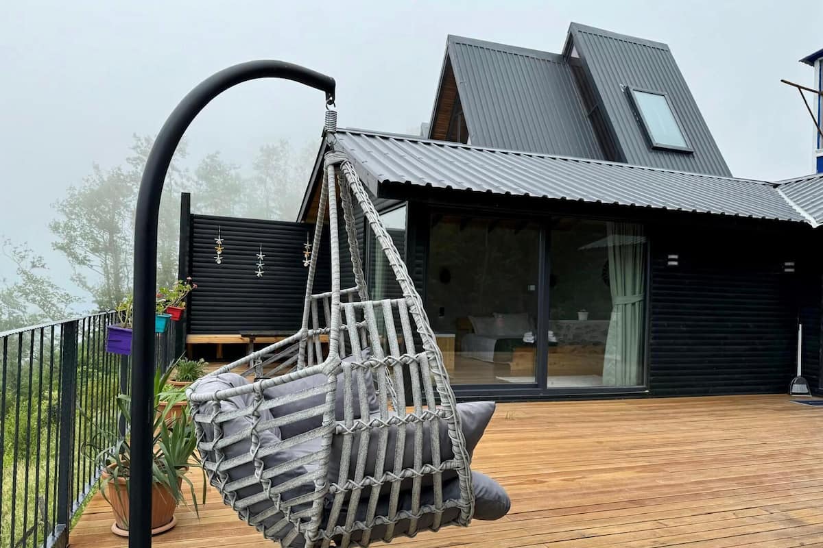 Ein modernes Haus mit einer Holzterrasse, einem Hängesessel und Blick auf die Umgebung.