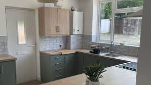 A modern kitchen with grey cabinets, a wooden countertop, and a window providing a view of the outdoors. - Hythe Hideaway - Home Away From Home (Hythe)
