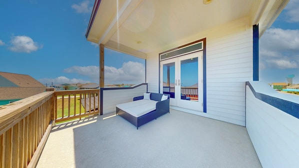 A balcony with a sofa, a wooden deck, and a view of the surrounding area.