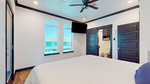 Une chambre à coucher avec un lit, un ventilateur de plafond, une télévision et une vue sur la plage par une fenêtre.