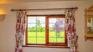 A window with floral curtains, a wooden frame, and a view of a green landscape. - Bluebells by STAE-Homes (Bristol)
