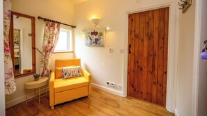 A room with a wooden floor, a yellow sofa, a small round table, a mirror, a wooden door, and a wall-mounted light fixture. - Lavender by STAE-Homes (Bristol)