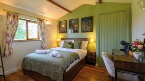 A bedroom with a wooden bed, green curtains, a desk with a chair, and artwork on the wall. - Rose by STAE-Homes Su (Bristol)