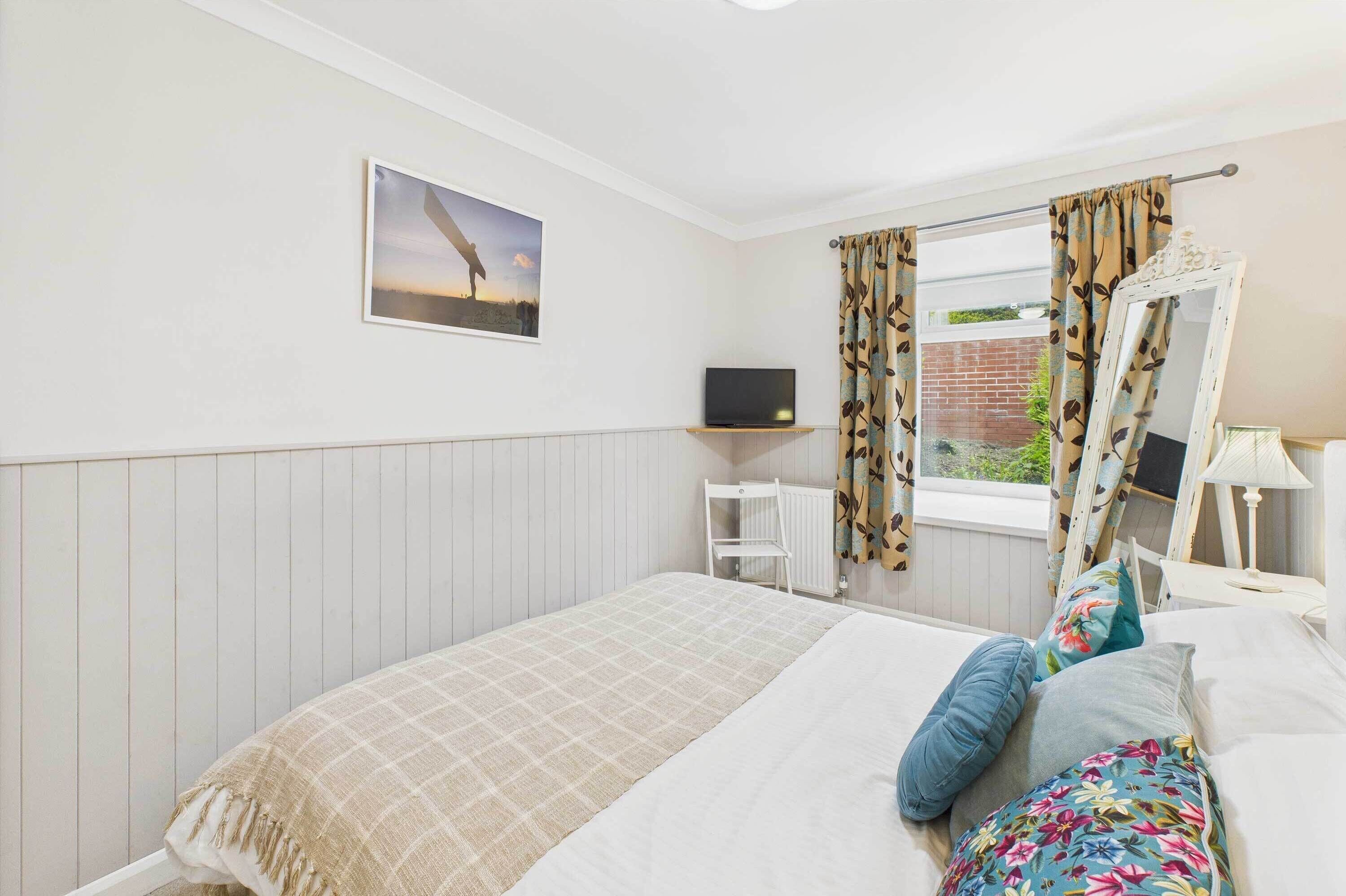 A bedroom with a bed, a television on a shelf, a window with curtains, and a mirror.