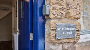 A stone wall with a sign reading "St. Cuthbert's Cottage." - Host & Stay | St Cuthbert's Cottage (Seahouses)