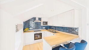 A compact kitchen with white cabinets, a wooden countertop, a blue backsplash, and a microwave. - Host & Stay | St Cuthbert's Cottage (Seahouses)