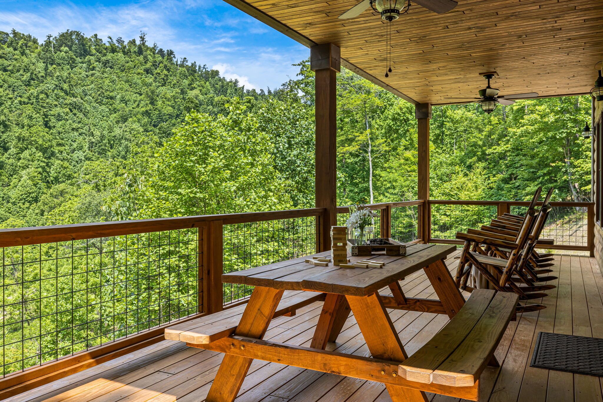 Una terraza de madera con mesas y sillas de picnic con vista a un paisaje boscoso.
