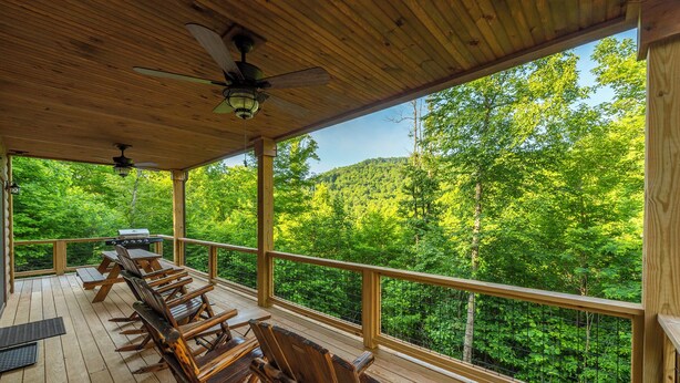 A wooden deck with outdoor seating, a grill, and a view of a forested hillside.