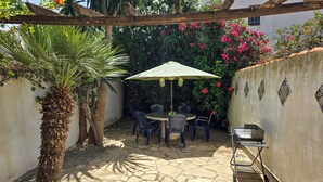 A patio area with a stone floor, a table with chairs, a wooden pergola, and a grill.