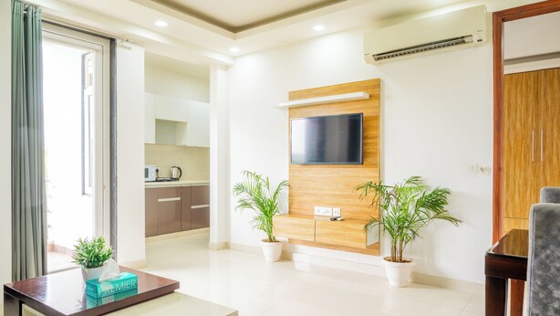 Una sala de estar moderna con un televisor de pantalla plana montado en un panel de madera, dos plantas en macetas, una cafetera y una mesa con una caja de pañuelos.