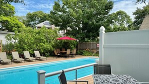 A swimming pool with lounge chairs and a table, surrounded by trees and a wooden fence. - Unique West Harwich Vacation Compound w/ Pool RPAM111 (West Harwich)