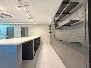 A modern kitchen with a long countertop, built-in bar stools, and a wall-mounted shelf unit.