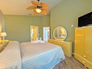 A hotel room with a bed, a vanity with a mirror, a television, and a ceiling fan.